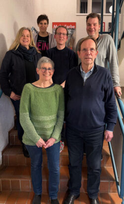 Sechs Menschen stehen in einer lockeren Gruppe auf einer Treppe und schauen von leicht oben in die Kamera.