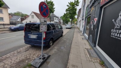 In einer Parkbucht an einer Straße steht ein Transporter. Vor der Parkbucht steht auf dem dortigen benutzungspflichtigen Radweg ein Halten-Verboten-Schild quer zur Fahrtrichtung. Unter dem Schild ein Hinweis, dass es am 13.04. gültig ist. Das Foto wurde am 06.05. aufgenommen.